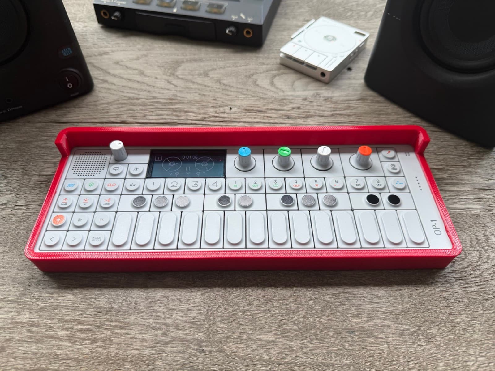 OP-1 in a Signal Red bumper on a studio desk between monitors